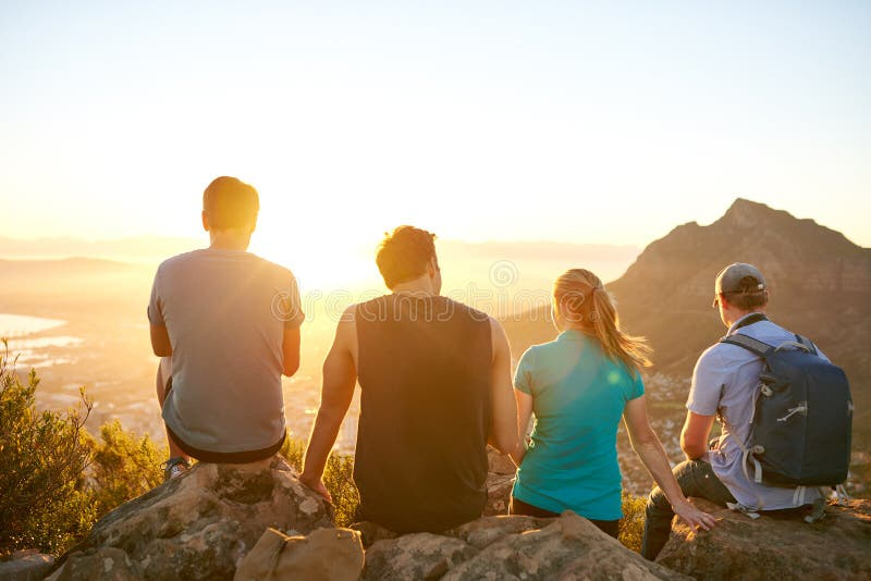Four friends sitting on a mountain top enjoying a sunrise view during a hike