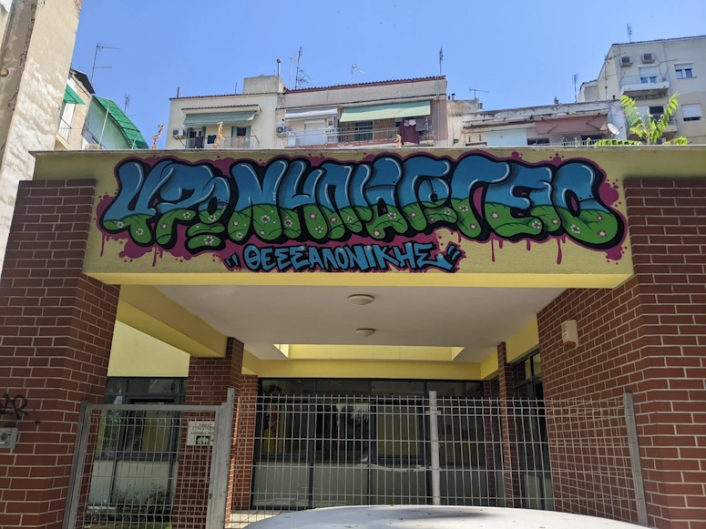 Street art mural reading ΘΕΣΣΑΛΟΝΙΚΗΣ above a building entrance, Thessaloniki