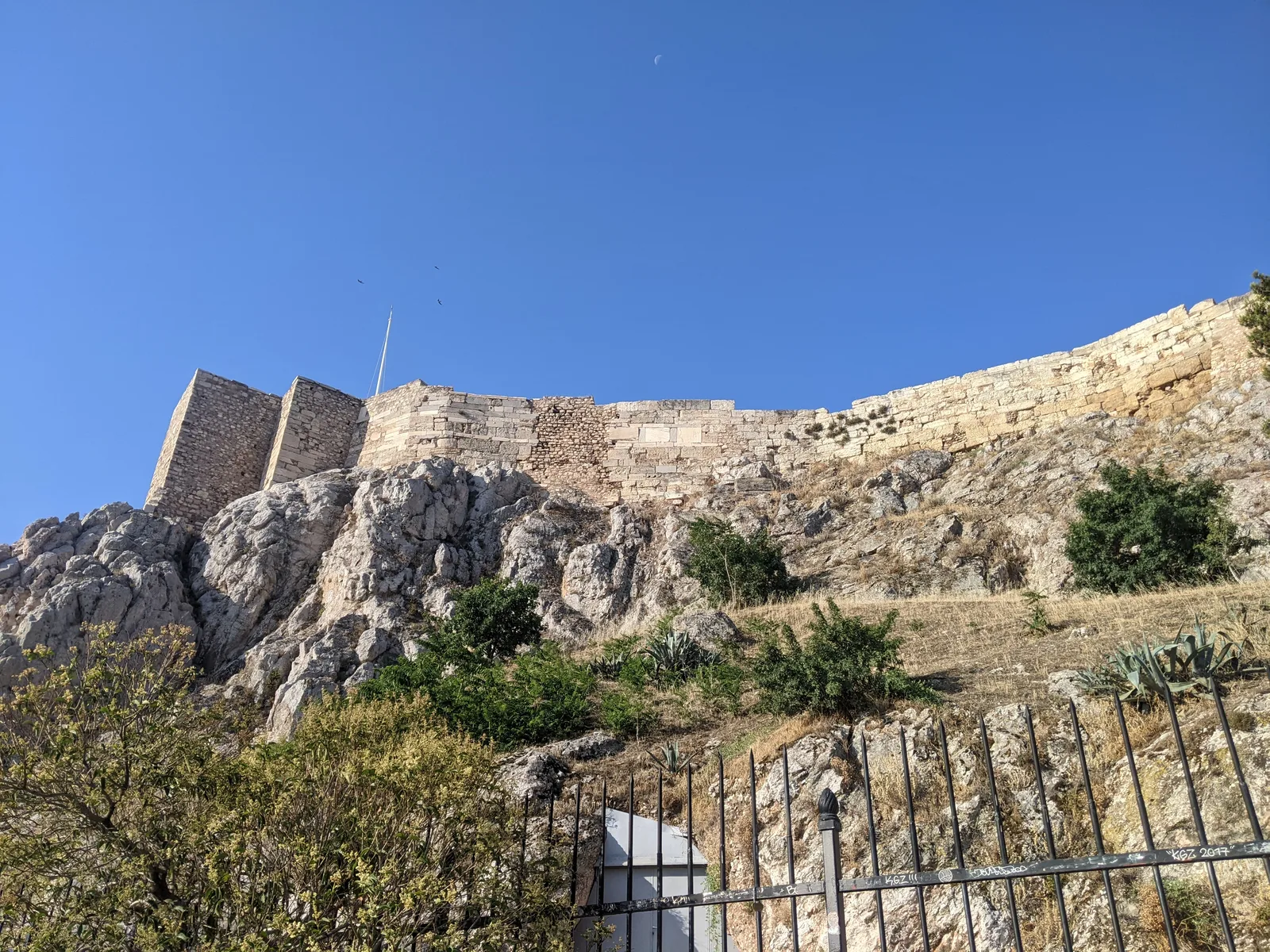 Acropolis walls and rocky hillside seen from a street below, Athens