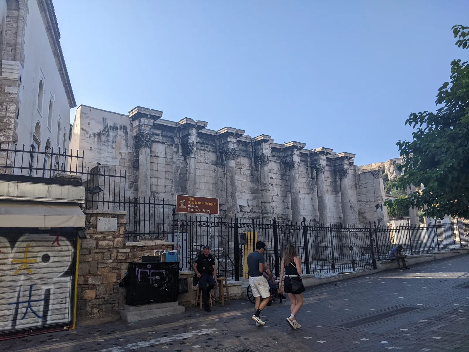 Street view of Hadrian's Library wall with pedestrians and the Acropolis visible behind, Athens