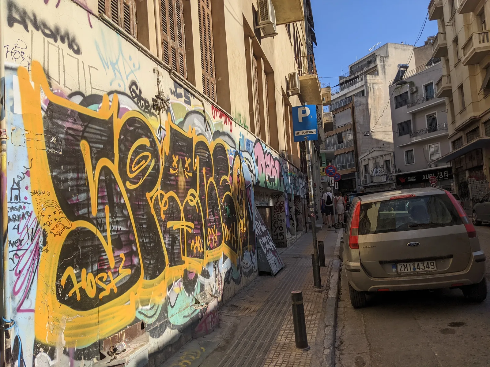 Athens side street with large graffiti covering an entire building wall, cars parked outside