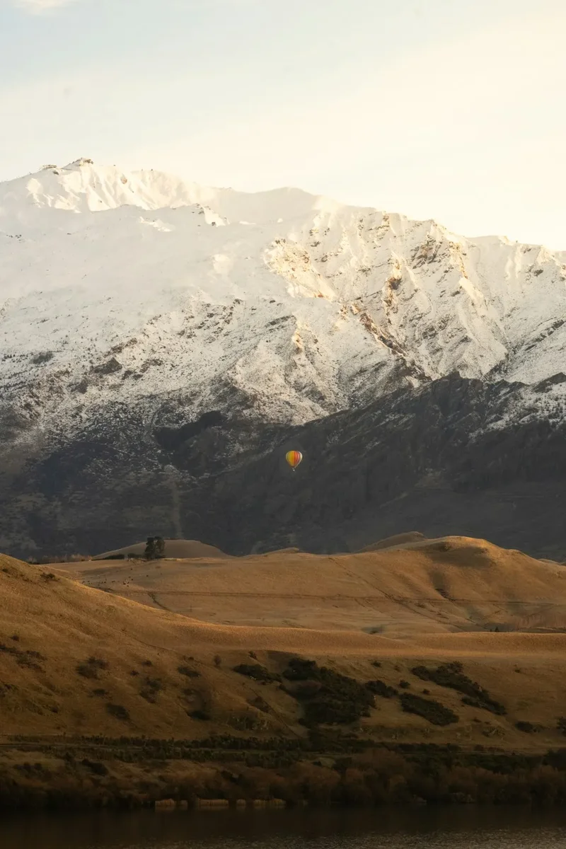 Hot air balloon floats near snow-capped mountains