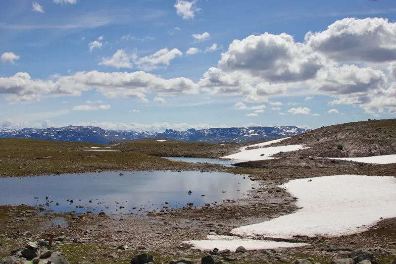 a lake surrounded by snow covered mountains under a blue sky