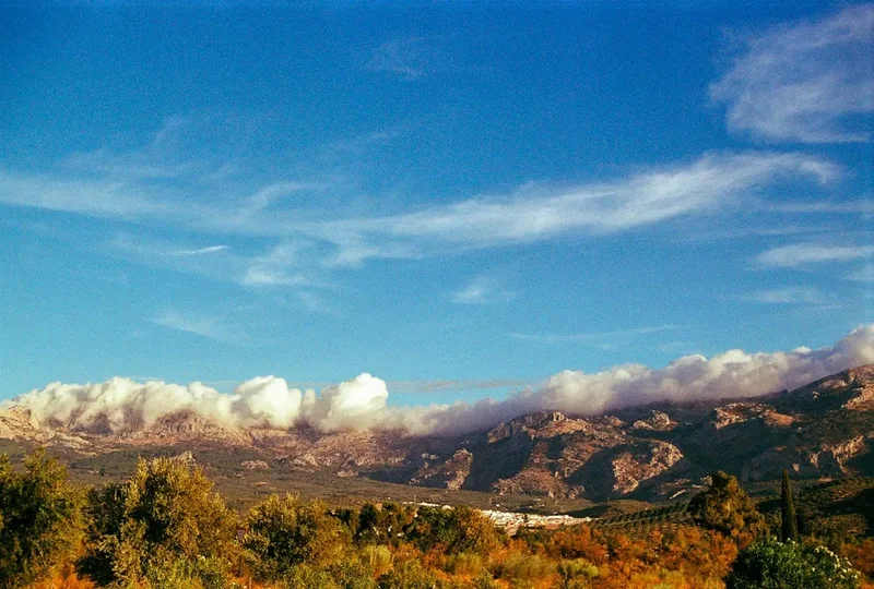 Clouds float above mountains and a clear sky.