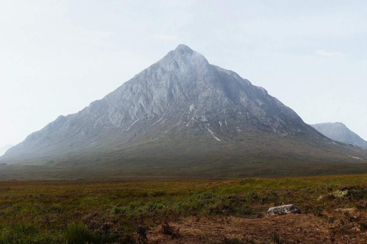A large mountain with a grassy field below it