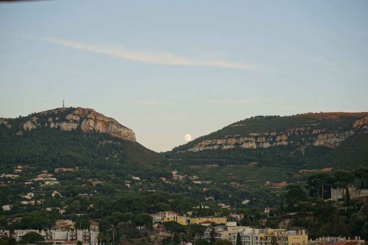 Moon visible between forested hills over a town.