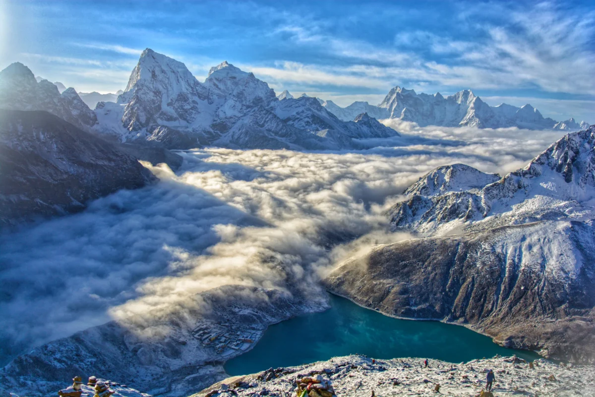 Snowy mountain peak amidst clouds and valley.