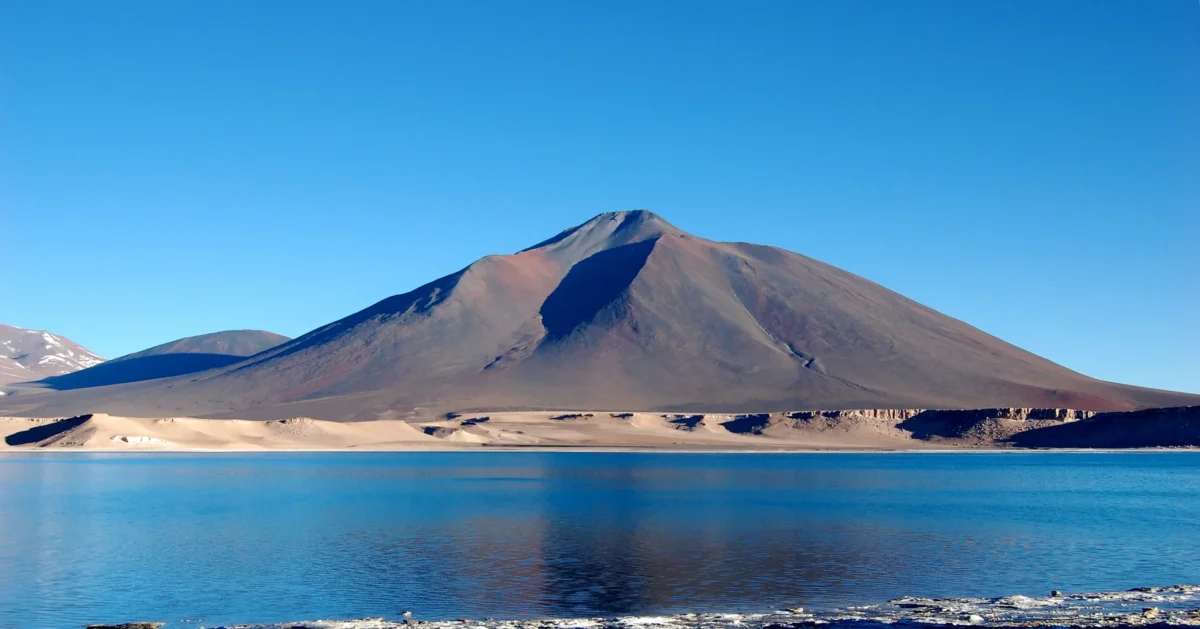 Red rocks in foreground with distant mountains and lake.
