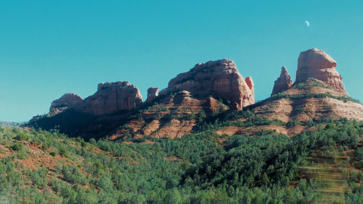 Red rock formations with green trees under blue sky.