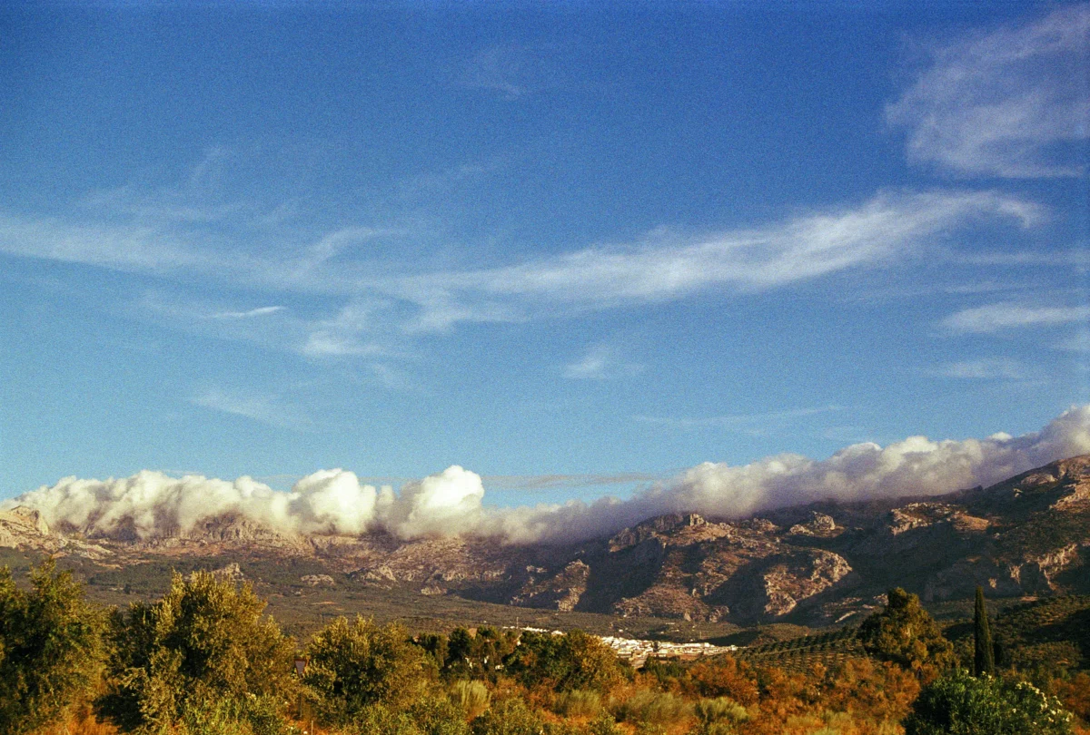 Clouds float above mountains and a clear sky.