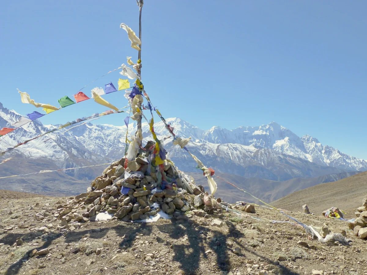 Prayer flags flutter on a cairn with snowy mountains behind