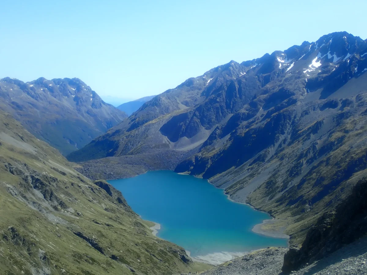 green and brown mountain beside lake under blue sky during daytime