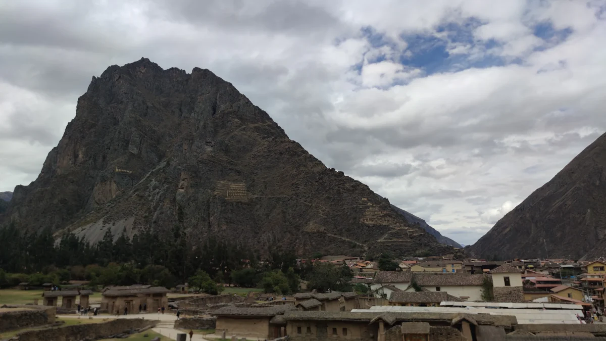 A large mountain overlooks a village under a cloudy sky