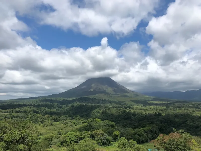 Volcano shrouded in clouds over lush green forest.