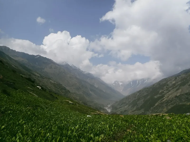 Green valley with mountains and clouds under blue sky