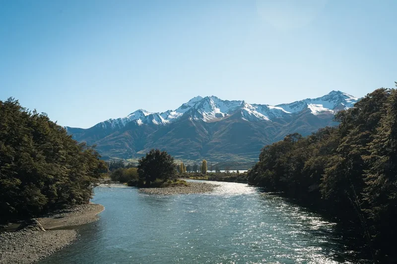 Snow-capped mountains rise above a wide river.
