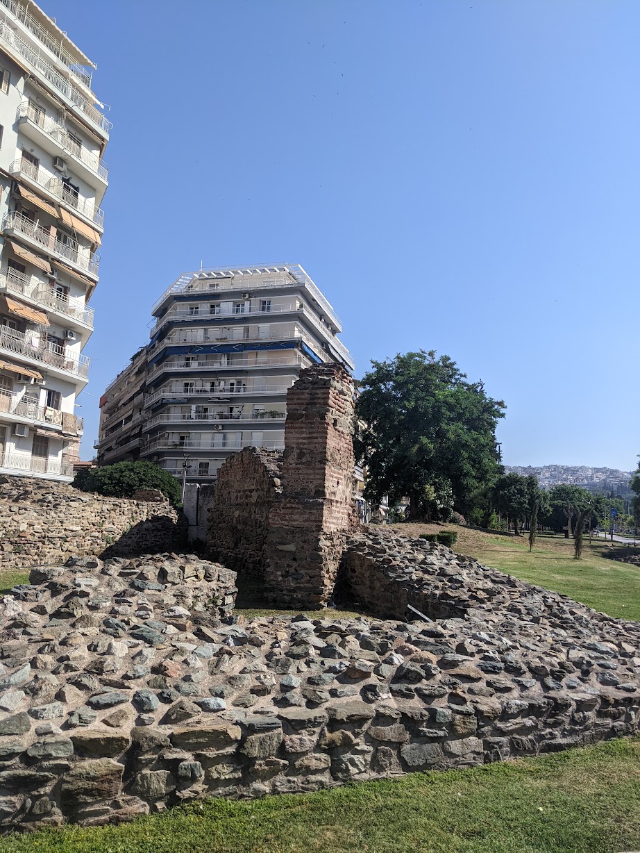 Brick-and-stone wall of the Palace of Galerius ruins with apartment buildings rising behind, Thessaloniki