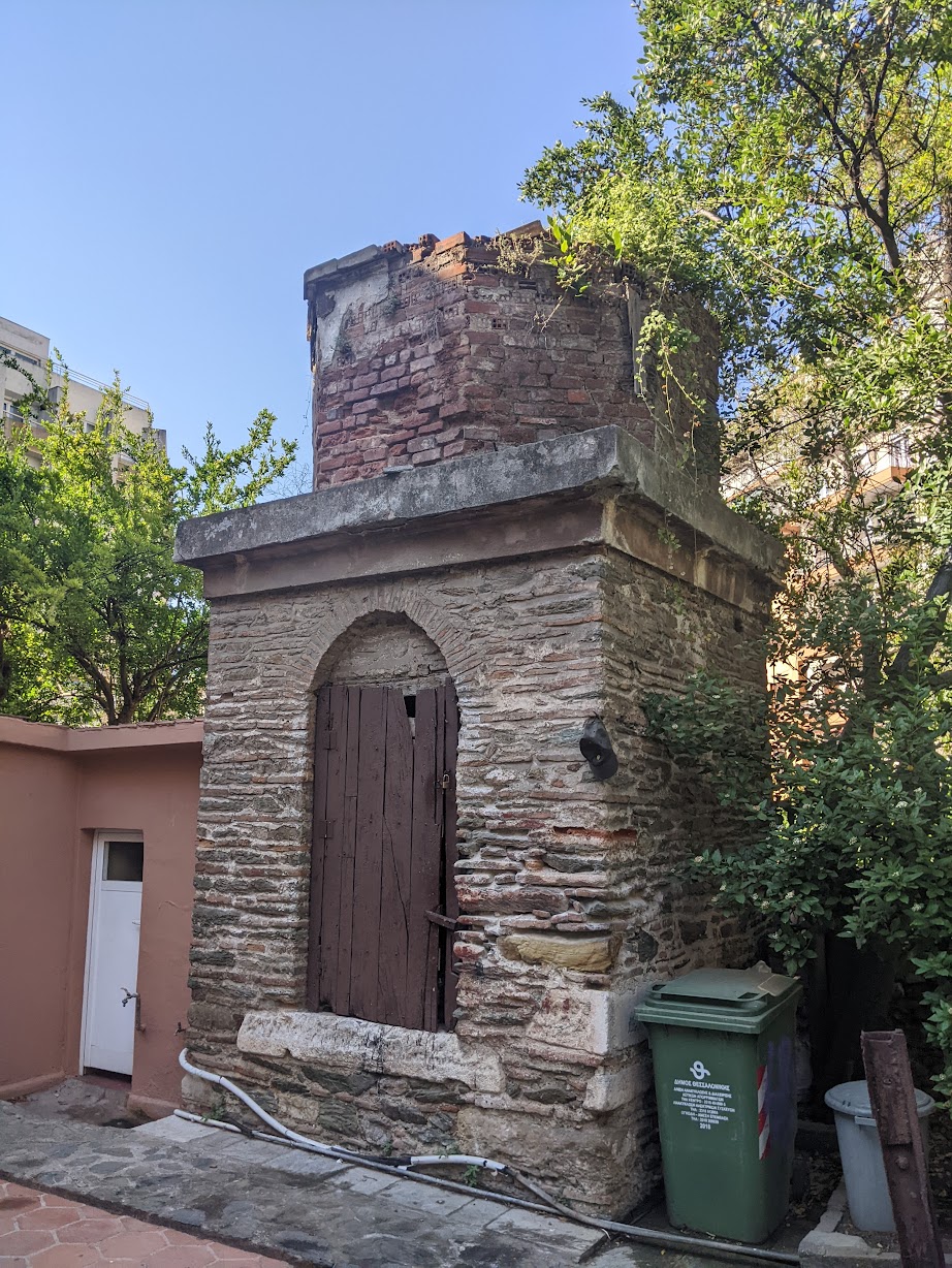 Restored Ottoman-era stone-and-brick fountain in Ano Poli, Thessaloniki, beside a wheelie bin