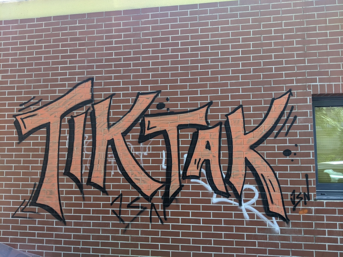 Orange TIK TAK graffiti piece on a red brick wall, Thessaloniki