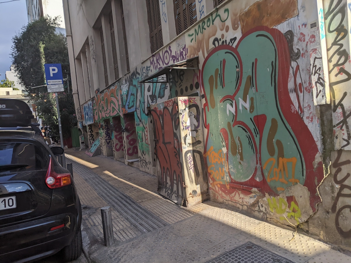 Layered graffiti along a sloping side street with parked cars, Thessaloniki