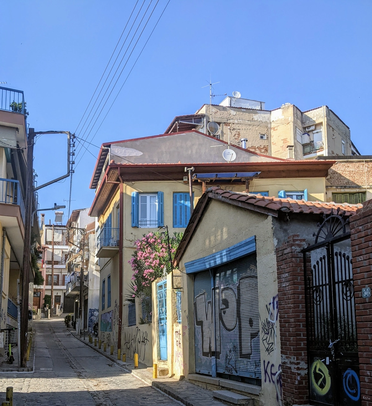 Cobblestone Ano Poli street with tagged shutters and traditional houses, Thessaloniki
