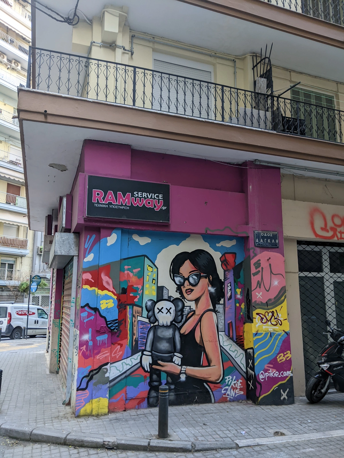 Street-corner mural of a woman holding a black KAWS-style figure by Pikie Cans, Thessaloniki