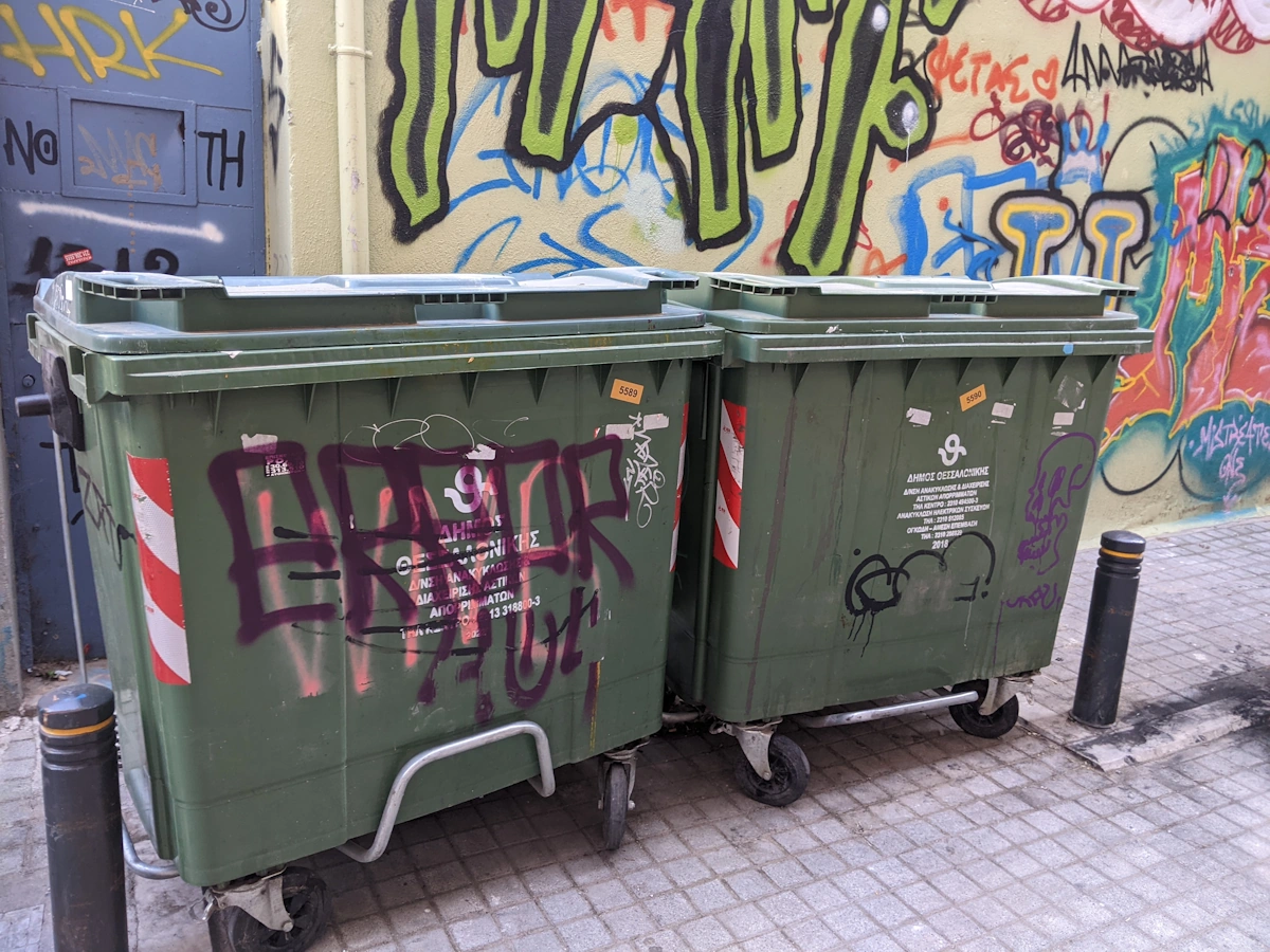 Tagged municipal rubbish bins in front of a graffiti-covered wall, Thessaloniki