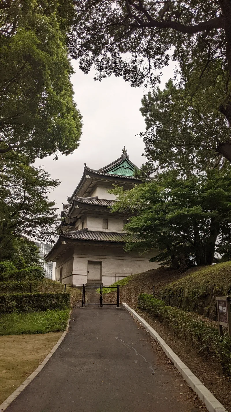 Leafy path leading to a white castle turret among trees in central Tokyo