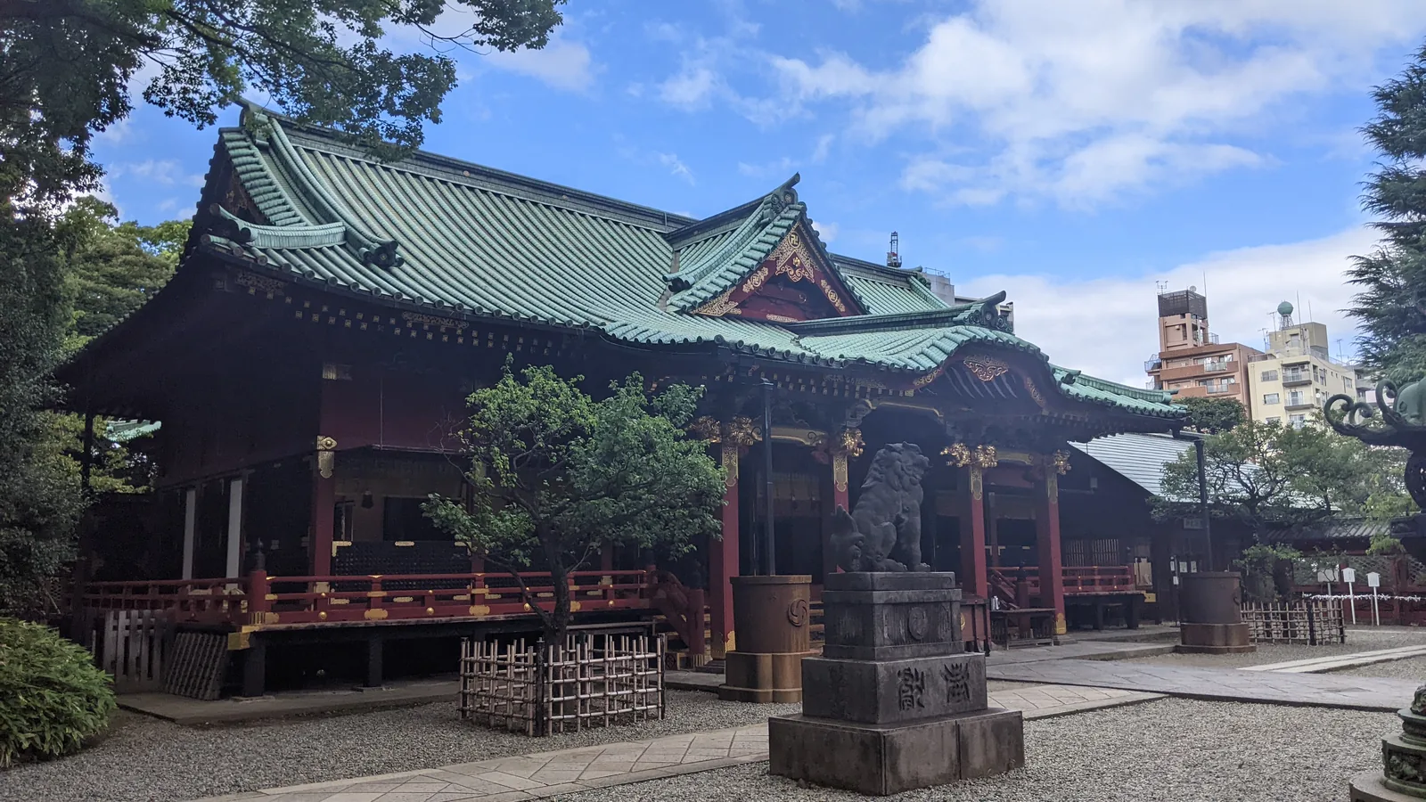 Green-roofed shrine building with vermilion trim beneath a blue sky in Tokyo
