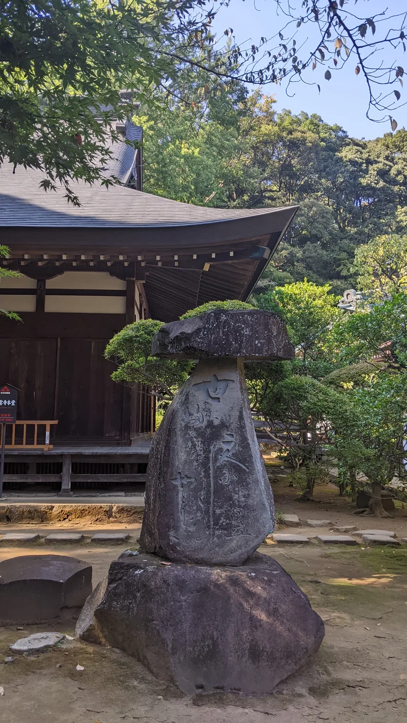 Weathered stone lantern in a temple garden with a wooden hall behind in Tokyo
