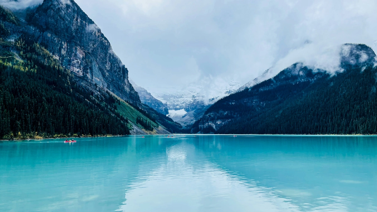 Turquoise waters of Lake Louise surrounded by snow-capped Rocky Mountain peaks with evergreen forests reflecting in the glacial lake