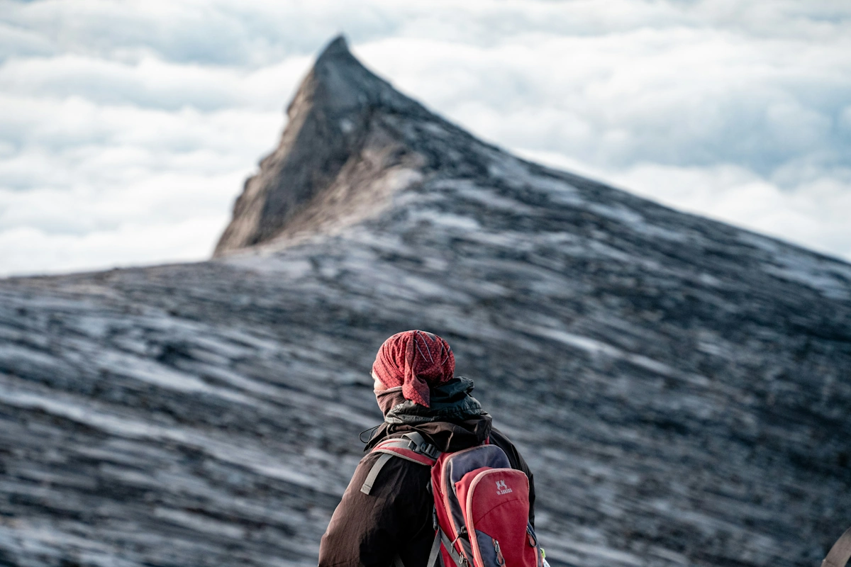 Hiker silhouetted at sunrise on Mount Kinabalu summit with dramatic mountain peaks and clouds in Sabah, Malaysia
