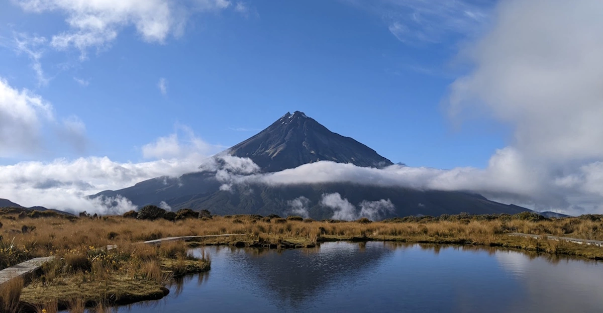 Mount Taranaki reflected in the Pouakai Tarns with alpine tussock grasslands in the foreground on New Zealand's Pouakai Circuit