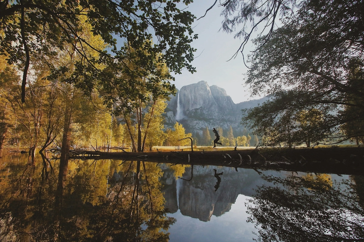 Yosemite Valley at sunrise with Yosemite Falls cascading down granite cliffs, meadows in the foreground, and dramatic mountain peaks